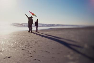 Silhouette of a father and son flying a kite on th